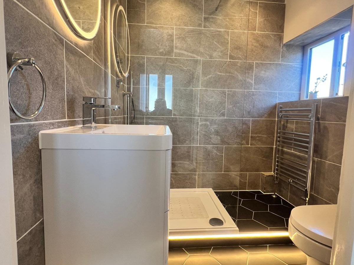Completed family bathroom refurbishment with marbled grey wall tiles, black hexagonal floor tiles and integrated LED plinth lighting