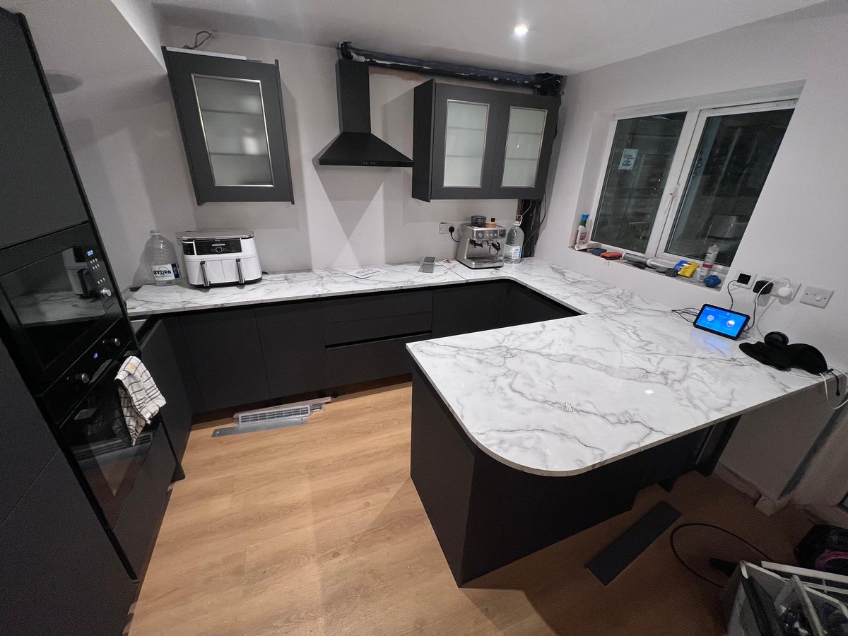 Completed Wren kitchen in dark graphite with marble-effect peninsula, integrated appliances and recessed ceiling speakers